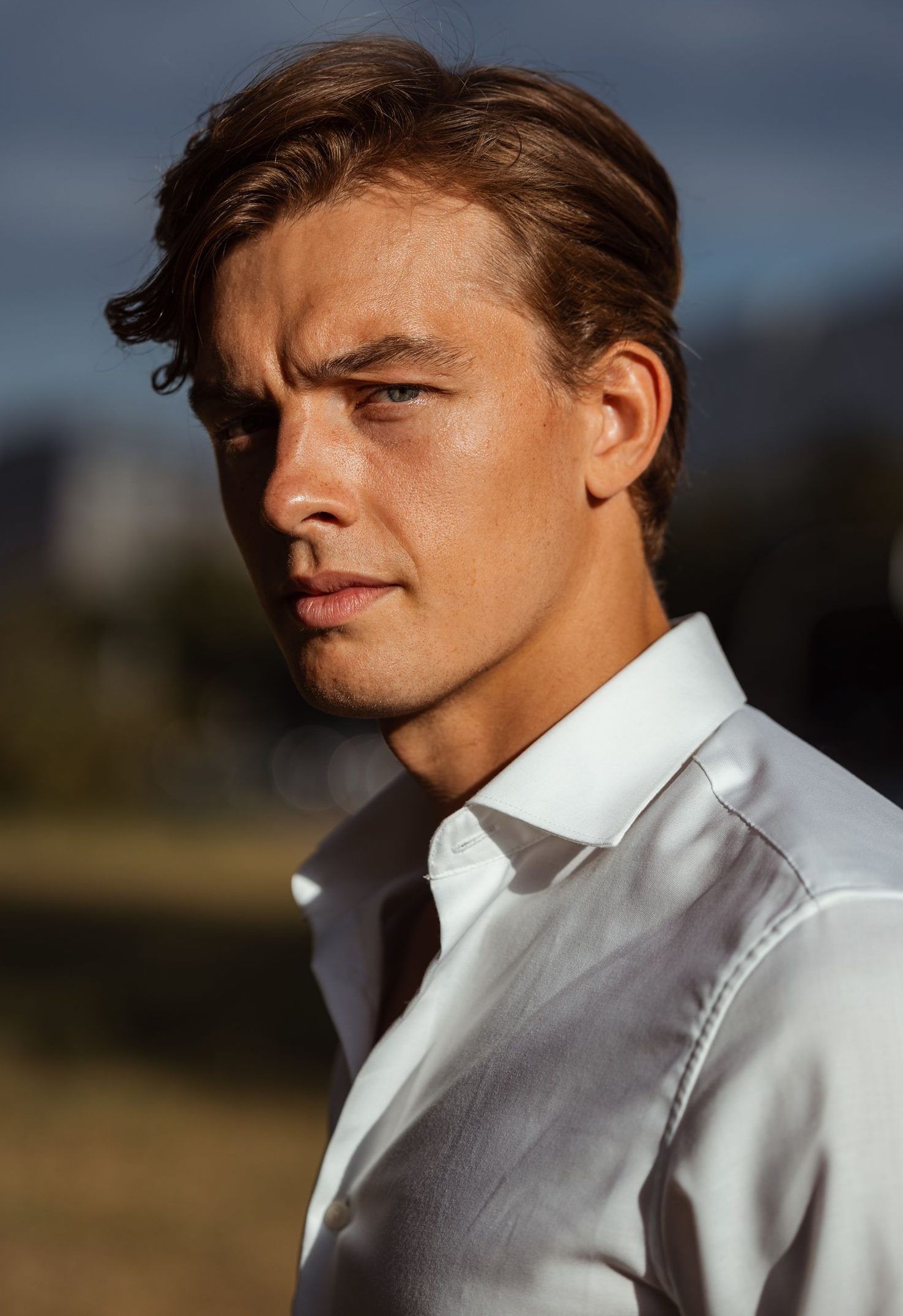 Portrait of a young man in a white shirt outdoors, looking pensive and confident.