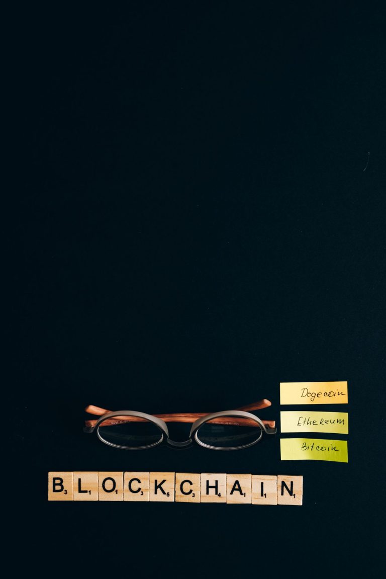 Scrabble tiles spelling blockchain, eyeglasses, and cryptocurrency notes on black background.