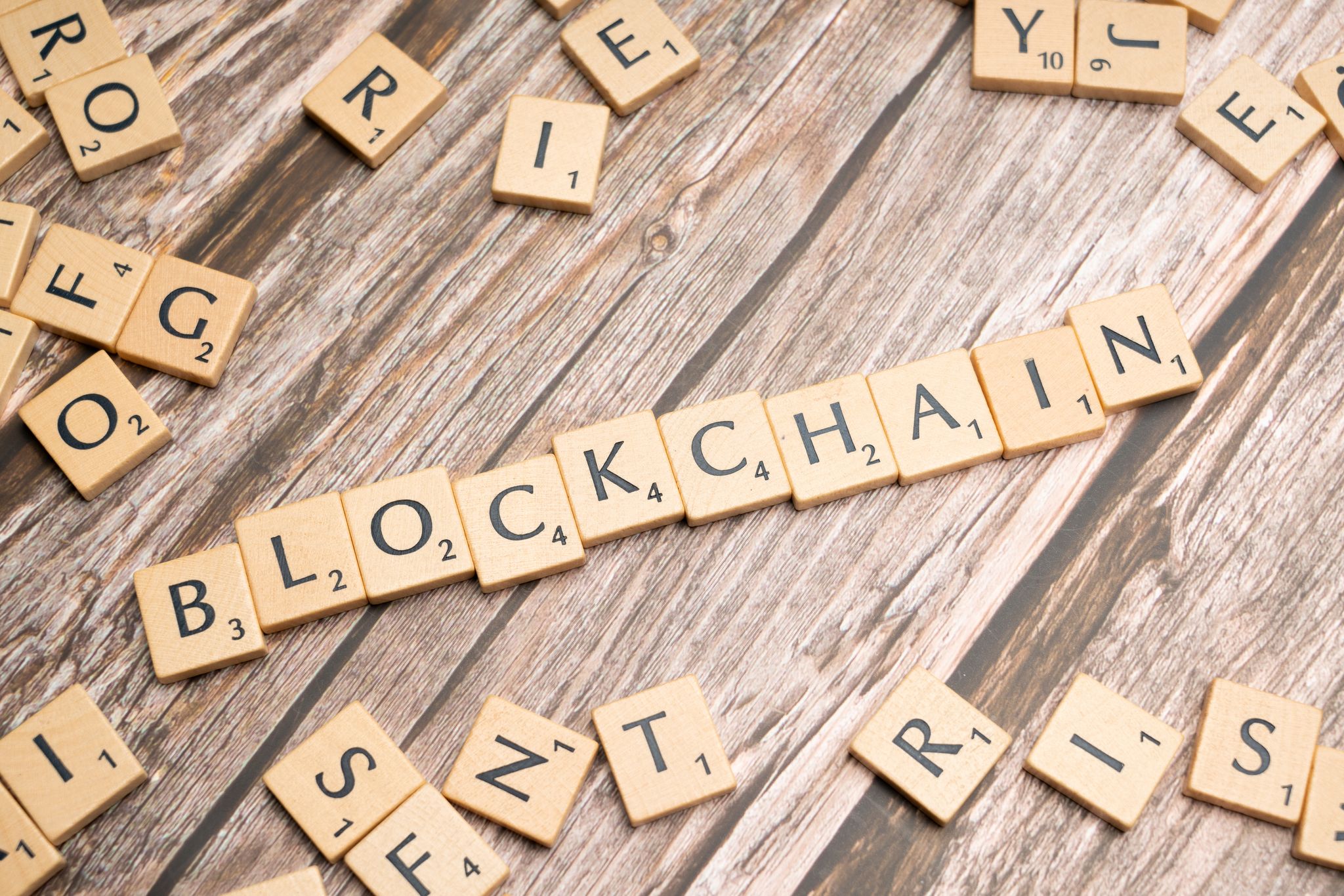 Wooden letter tiles form the word 'blockchain' arranged on a rustic wood background.